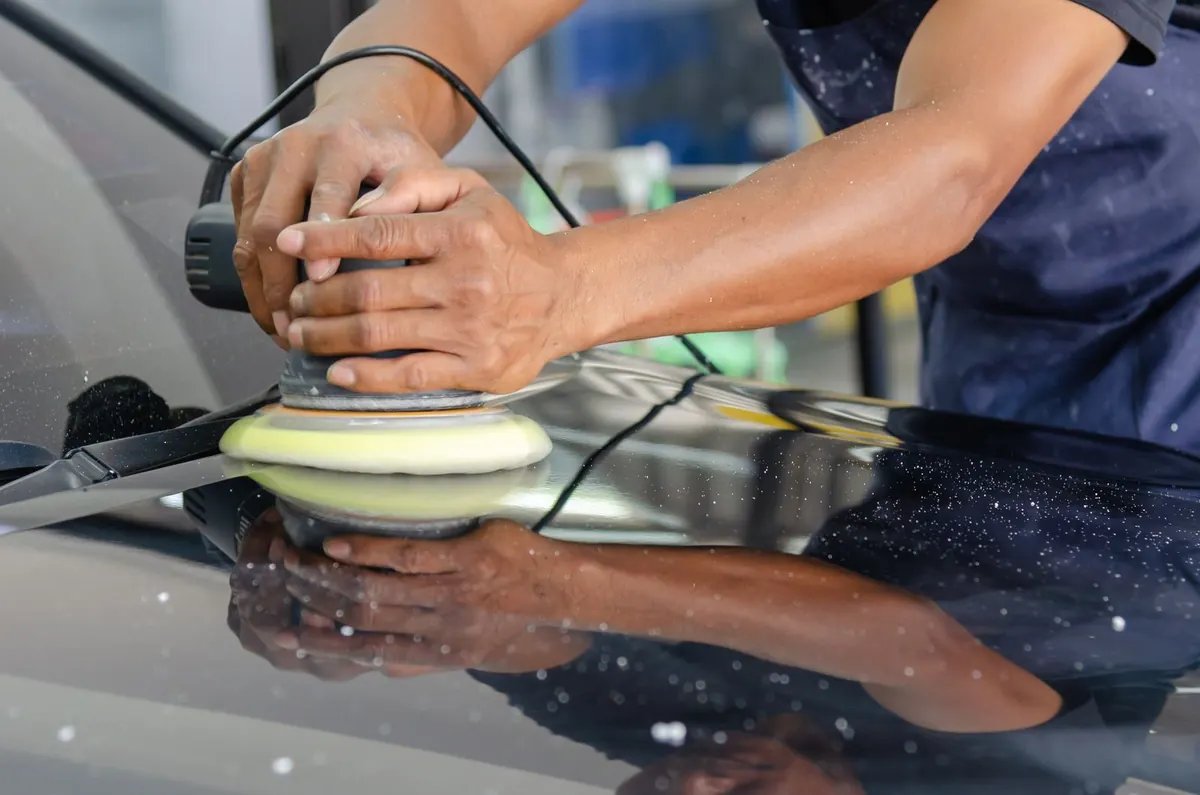 Hands guiding a machine polisher across a car hood.