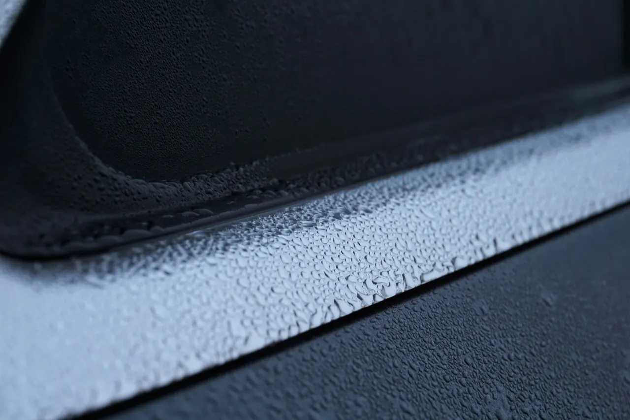 Water droplets beading on a car's gray painted body panel.
