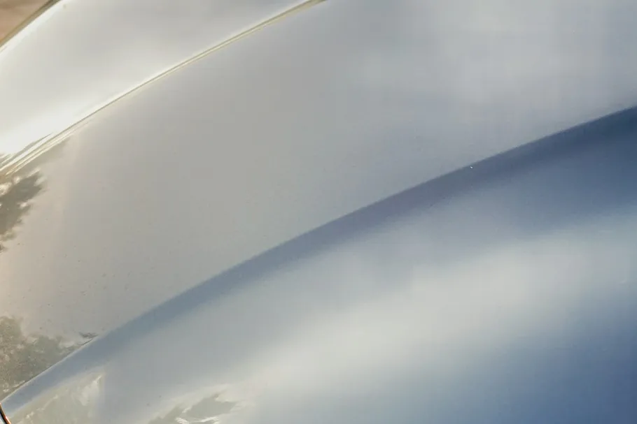 Glossy car paint reflecting light and trees.