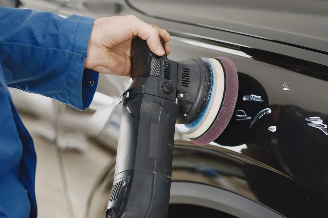 Hands guiding a polishing machine over a car's painted surface.