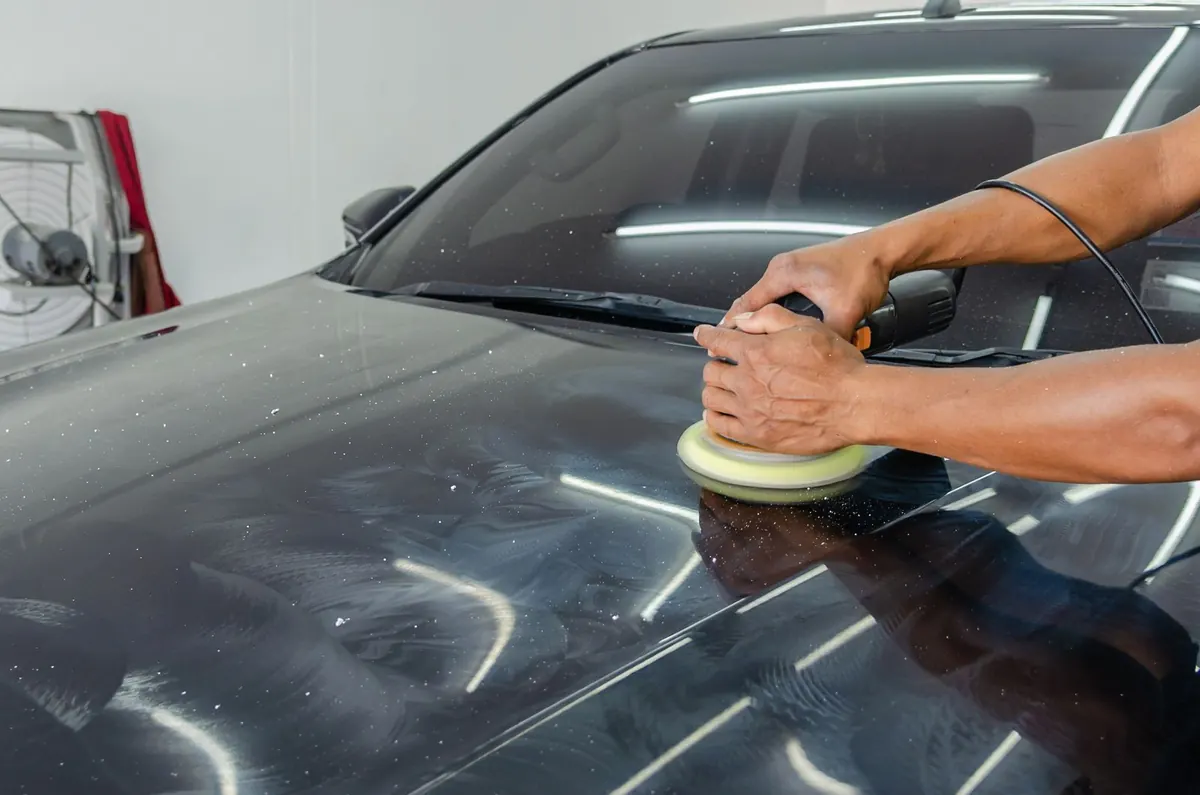 Hands guiding a polishing machine across dark car paint.