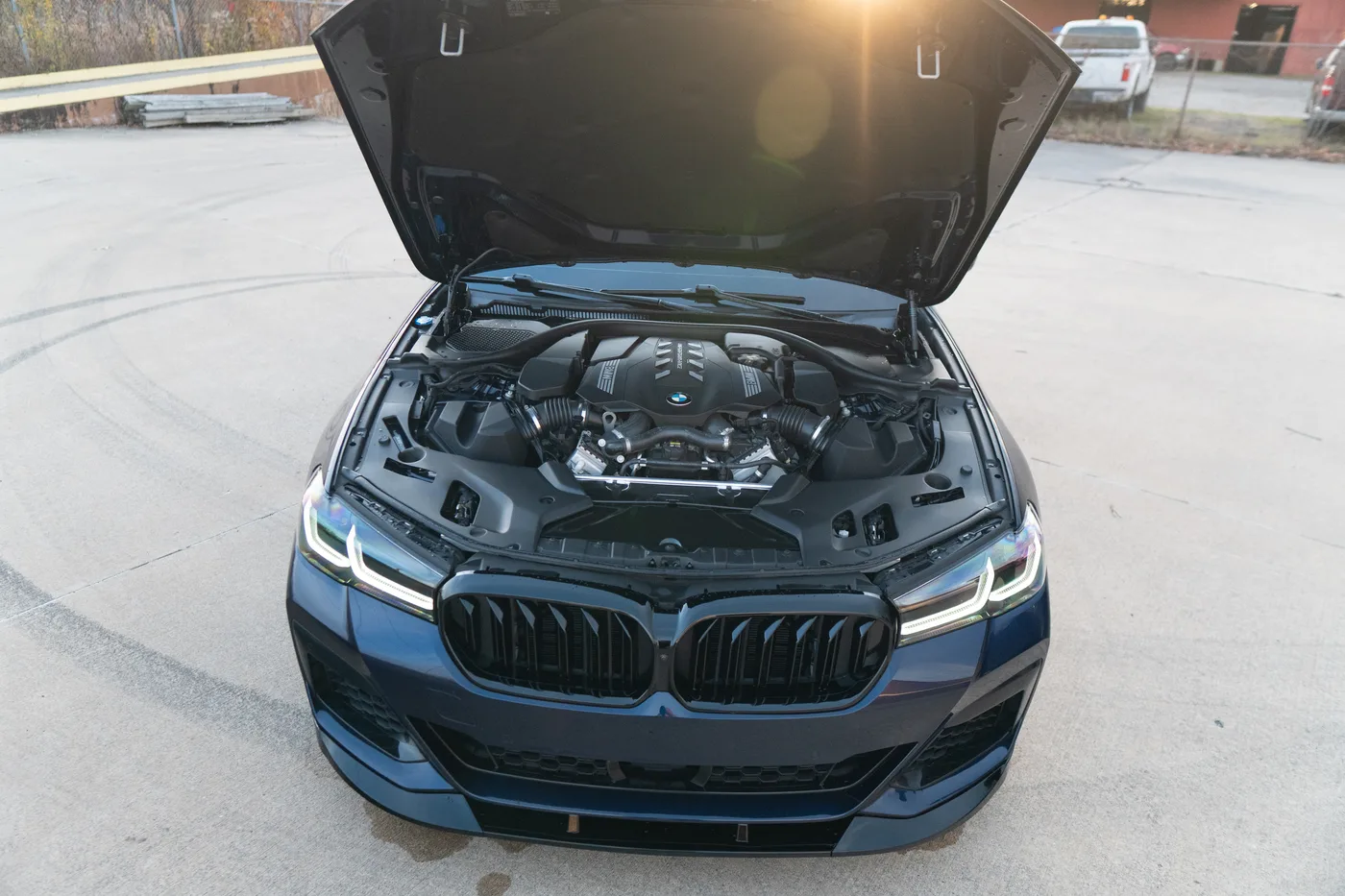 A blue BMW M5 with the hood open in low sun